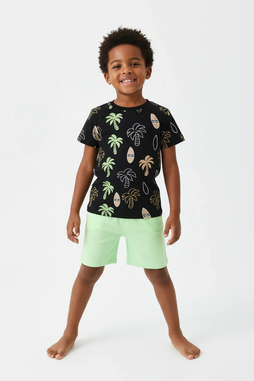 	Garçon debout en ensemble palmiers tropicaux BabyCoton — t-shirt noir all-over palmiers planches surf et short vert fluo, fond blanc