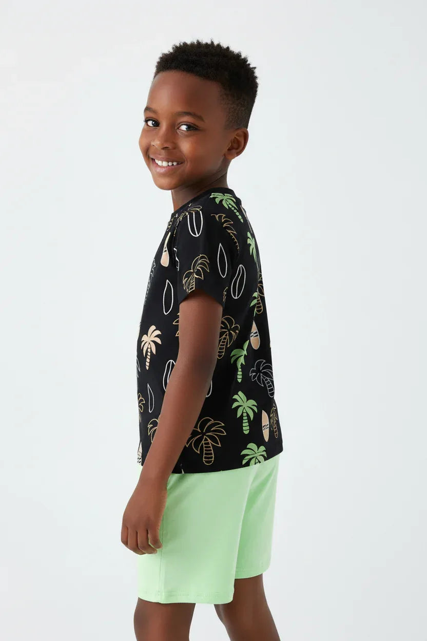 Vue 3/4 dos garçon se retournant souriant — ensemble palmiers tropicaux BabyCoton, t-shirt noir all-over palmiers surf et short vert fluo, fond blanc

