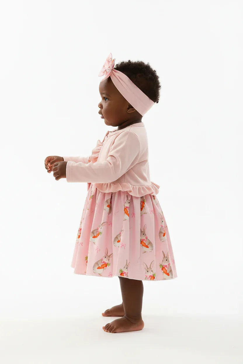 	Vue de profil bébé fille en ensemble rose BabyCoton — silhouette complète cardigan volants, jupe plissée lapins carottes et bandeau nœud, fond blanc