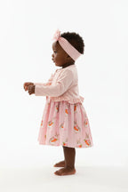 	Vue de profil bébé fille en ensemble rose BabyCoton — silhouette complète cardigan volants, jupe plissée lapins carottes et bandeau nœud, fond blanc