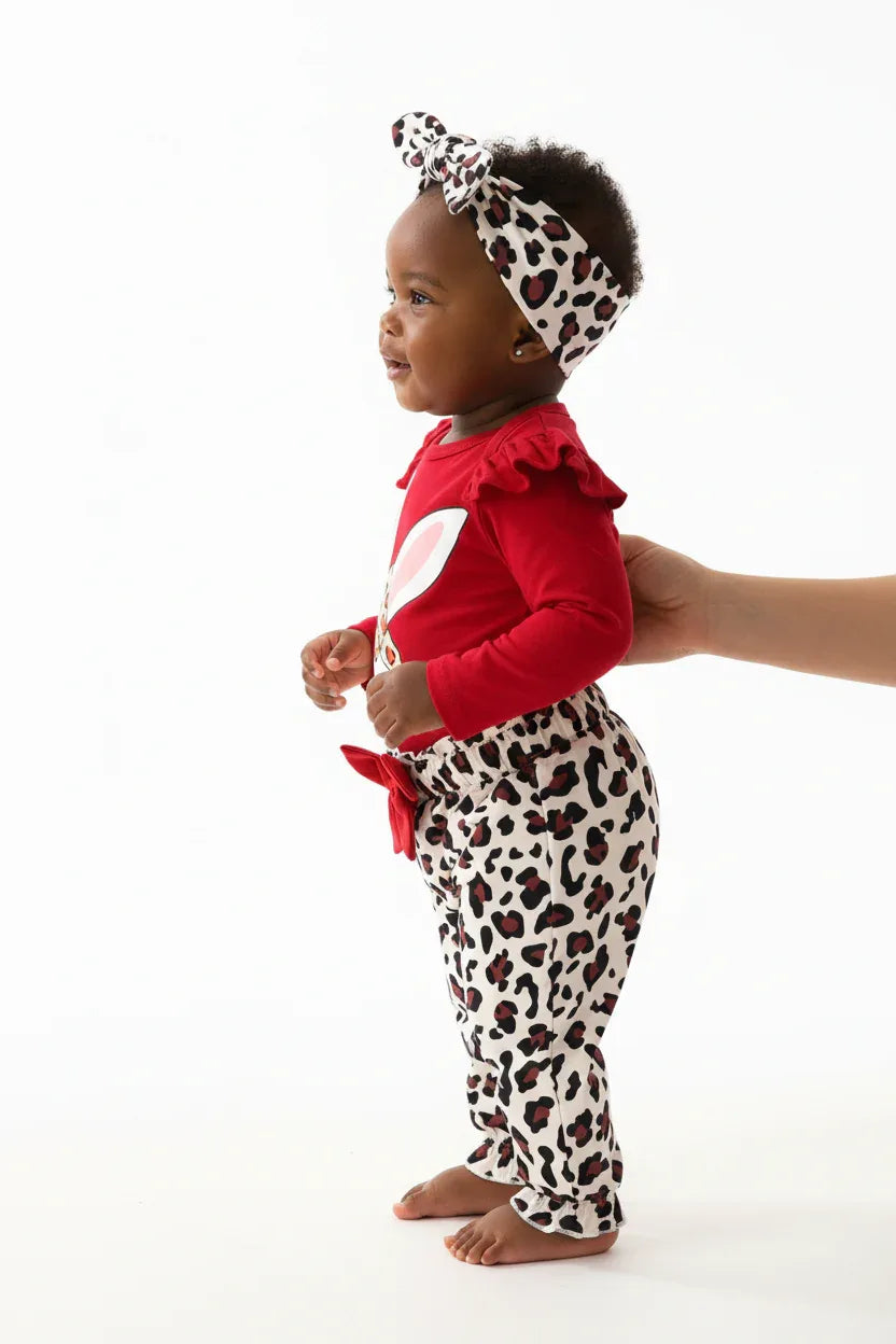 Vue de profil bébé fille en ensemble rouge BabyCoton — silhouette complète body lapin volants, pantalon léopard nœud rouge et bandeau léopard, fond