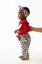 Vue de profil bébé fille en ensemble rouge BabyCoton — silhouette complète body lapin volants, pantalon léopard nœud rouge et bandeau léopard, fond
