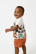 Vue de dos bébé garçon en ensemble dinosaures palmiers BabyCoton — chemise polo beige imprimée et short terracotta, fond blanc