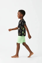 Vue de profil garçon en marche — ensemble palmiers tropicaux BabyCoton, t-shirt noir palmiers surf et short vert fluo, fond blanc