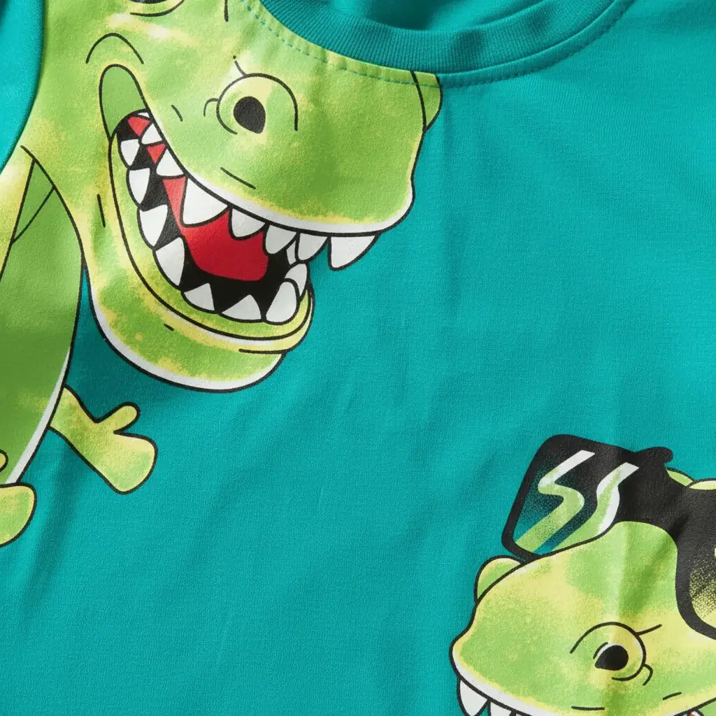 	Détail gros plan imprimé dinosaures cartoon — grand T-rex vert et petit dino lunettes noires sur t-shirt turquoise BabyCoton, fond blanc