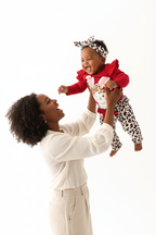 Maman soulevant bébé fille en ensemble rouge BabyCoton — body lapin rouge volants, pantalon léopard nœud rouge et bandeau, moment de joie fond blanc