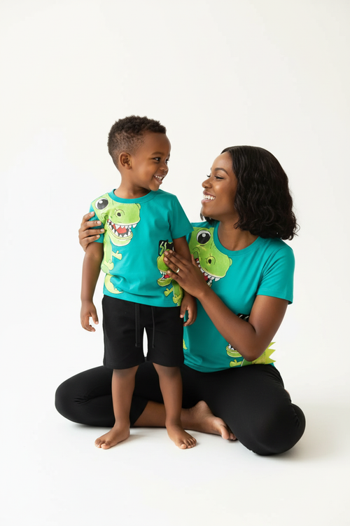 Maman et garçon moment complice — ensemble dinosaures turquoise BabyCoton, t-shirt T-rex lunettes et short noir uni, fond blanc