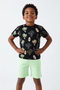 Angle bas garçon pose assurée — ensemble palmiers tropicaux BabyCoton, t-shirt noir all-over et short vert fluo, fond blanc