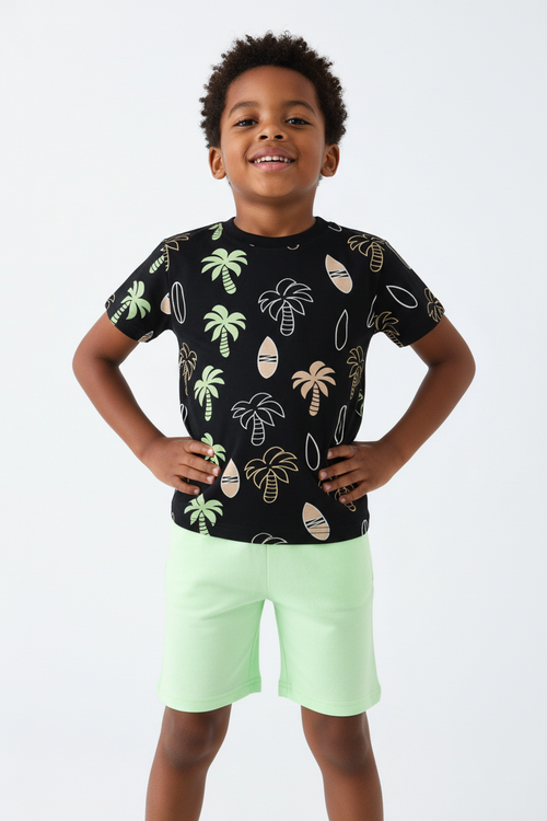 Angle bas garçon pose assurée — ensemble palmiers tropicaux BabyCoton, t-shirt noir all-over et short vert fluo, fond blanc