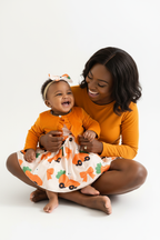 Maman et bébé fille riant ensemble en ensemble orange BabyCoton — cardigan volants, robe imprimée carottes et bandeau nœud, moment de joie fond blanc