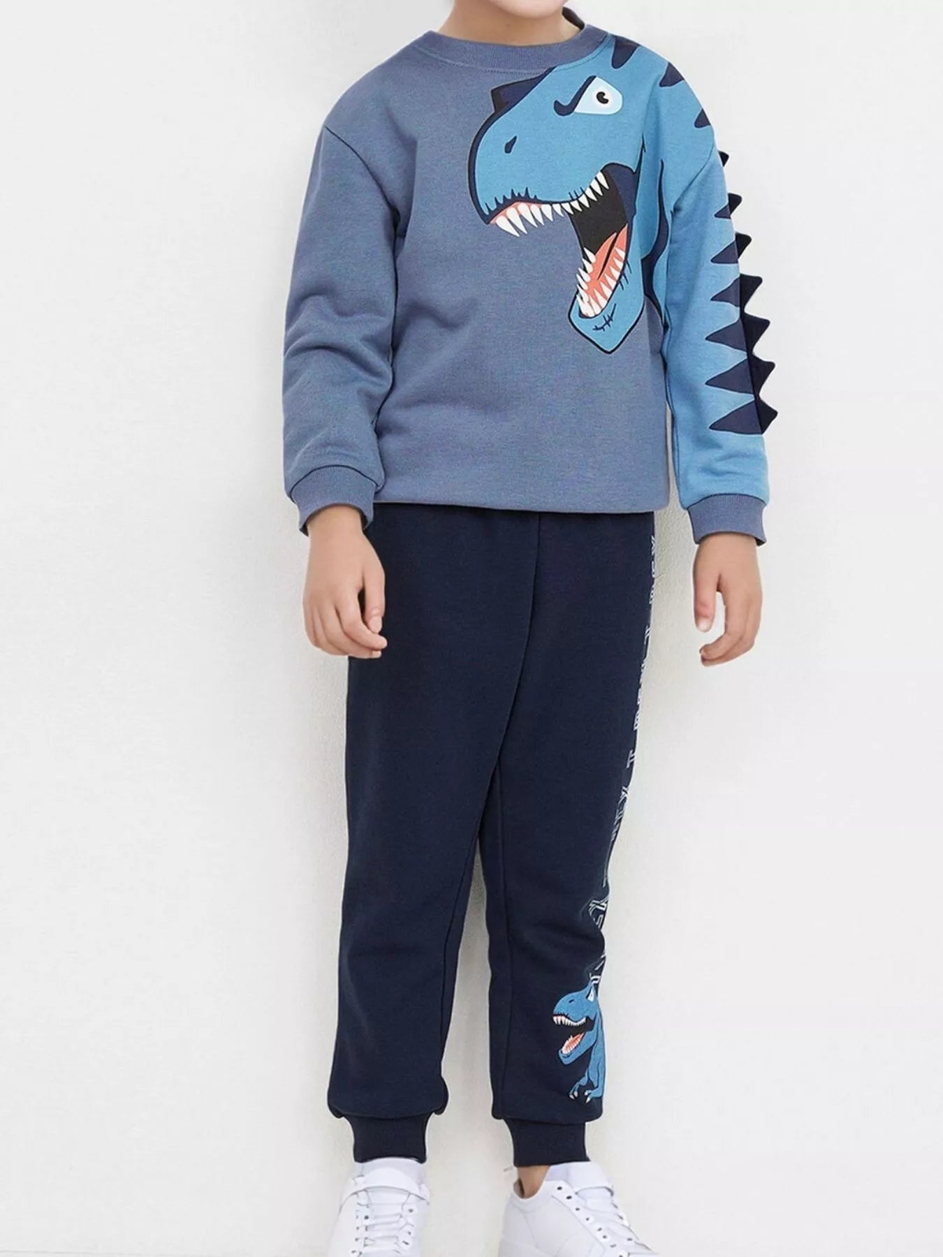 🦕 Enfant portant un ensemble sweat imprimé dinosaure coloré et pantalon assorti - vue de face montrant les T-Rex et Tricératops vibrants qui éveillent l'imagination des petits paléontologues