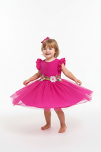 Fille en robe tulle fuchsia manches volantées - pose pirouette montrant le mouvement du tulle vaporeux - BabyCoton