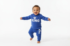 Bébé garçon d'origine diverse debout ou faisant ses premiers pas en portant un body hoodie bleu avec texte KING et couronne blanc et pantalon bleu assorti
