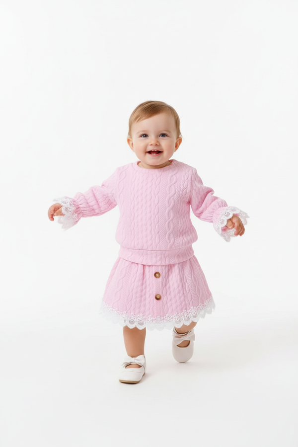 Bébé fille debout ou faisant ses premiers pas en portant l'ensemble haut dentelle rose et jupe - vue trois-quarts - fond blanc studio