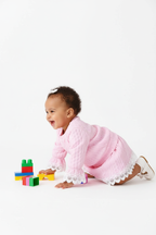 Bébé fille jouant activement en portant l'ensemble haut dentelle rose et jupe - vue de profil - fond blanc studio