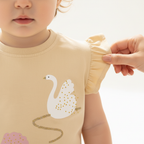 Détail broderie cygne sur top bébé fille — manches volantées coton beige, finitions artisanales qualité premium