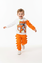 « Enfant en ensemble dinosaure orange et blanc sautant bras levés - vue de profil
