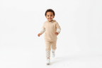 Enfant d'origine diverse courant joyeusement en portant un ensemble sweat à capuche beige avec détails à carreaux blancs et pantalon coordonné
