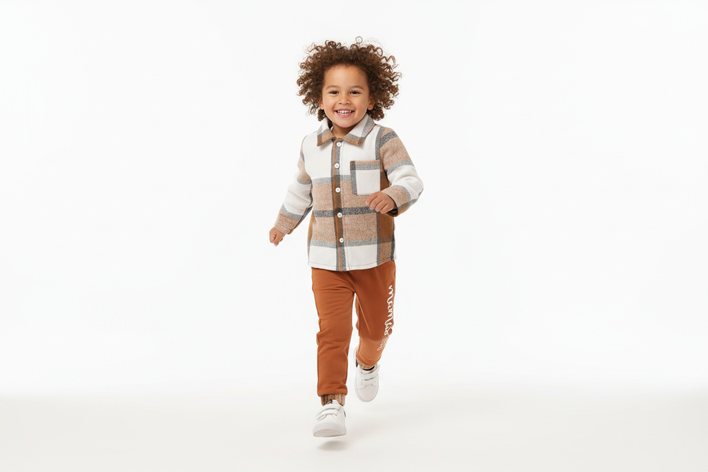 Garçon d'origine diverse courant joyeusement en portant une chemise boutonnée à carreaux beige et blanc avec pantalon orange
