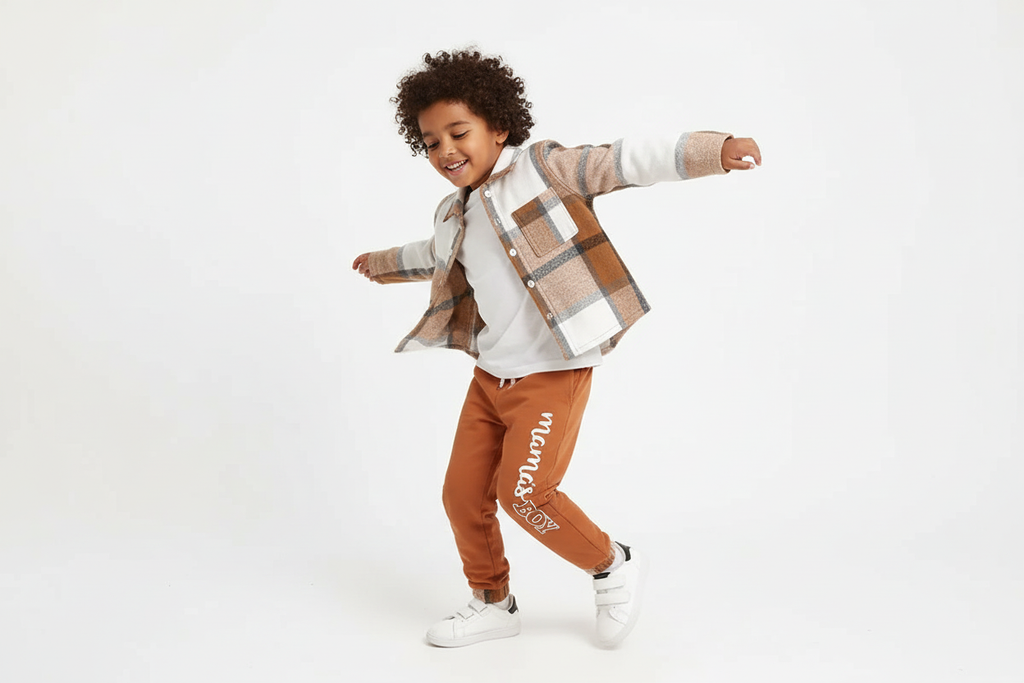 Garçon d'origine diverse dansant avec bonheur en portant une chemise boutonnée à carreaux beige et blanc avec pantalon orange

