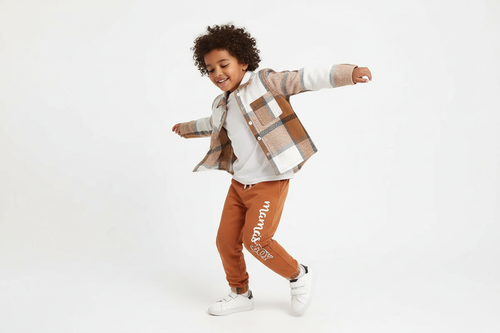 Garçon d'origine diverse dansant avec bonheur en portant une chemise boutonnée à carreaux beige et blanc avec pantalon orange

