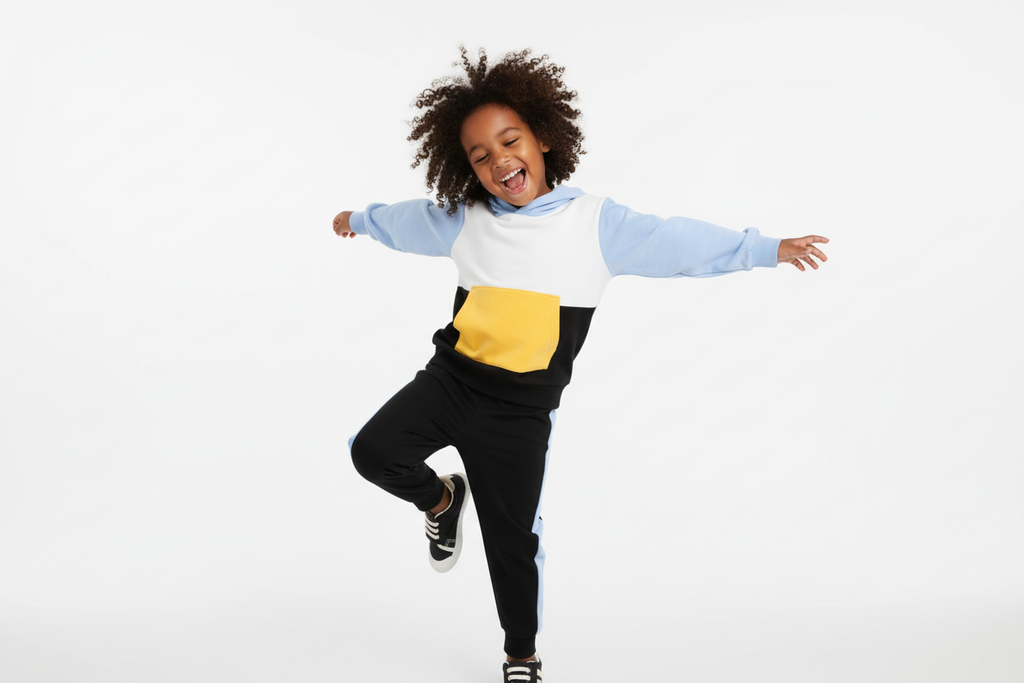 Enfant  dansant avec bonheur en portant un hoodie color block blanc, bleu ciel, jaune et noir avec pantalon noir à bandes bleues
