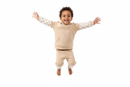 Enfant d'origine diverse sautant en l'air avec joie en portant un ensemble sweat à capuche beige avec motifs à carreaux et pantalon assorti
