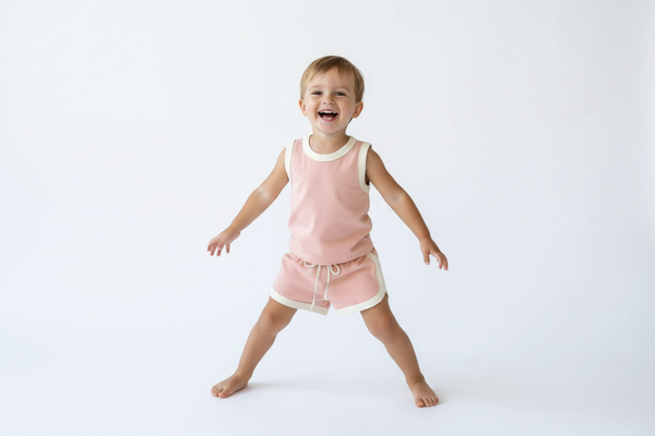 "Enfant faisant des mouvements sportifs portant un ensemble loisirs rose poudré avec détails blancs : débardeur + short avec cordon de serrage 🎀 - tenue confortable en coton pour activités physiques, jeux au parc et moments détente, tailles 66-120cm chez BabyCoton 💕"