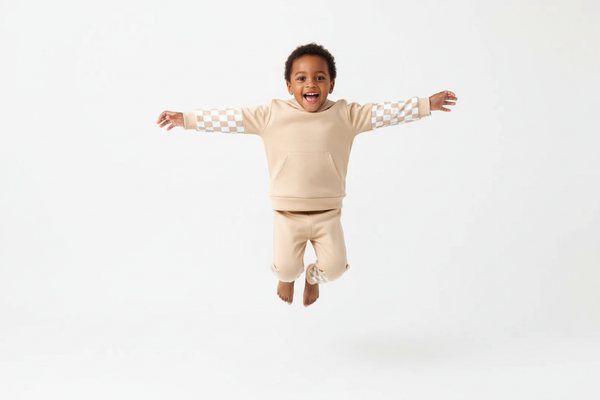 Enfant  sautant en l'air avec joie en portant un ensemble sweat à capuche beige avec motifs à carreaux et pantalon assorti
