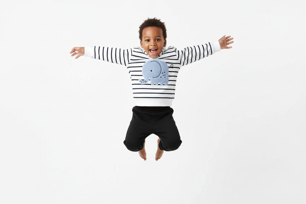 Enfant  sautant en l'air avec joie en portant un hoodie blanc à rayures noires avec appliqué éléphant bleu et pantalon noir
