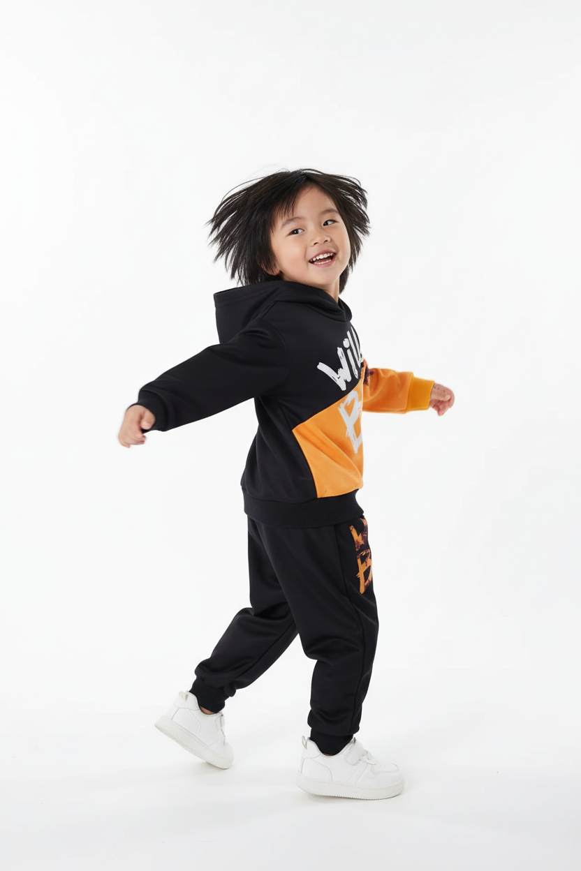 « Enfant accroupi en pose énergique portant sweat à capuche Wild Boy noir et orange avec pantalon assorti »