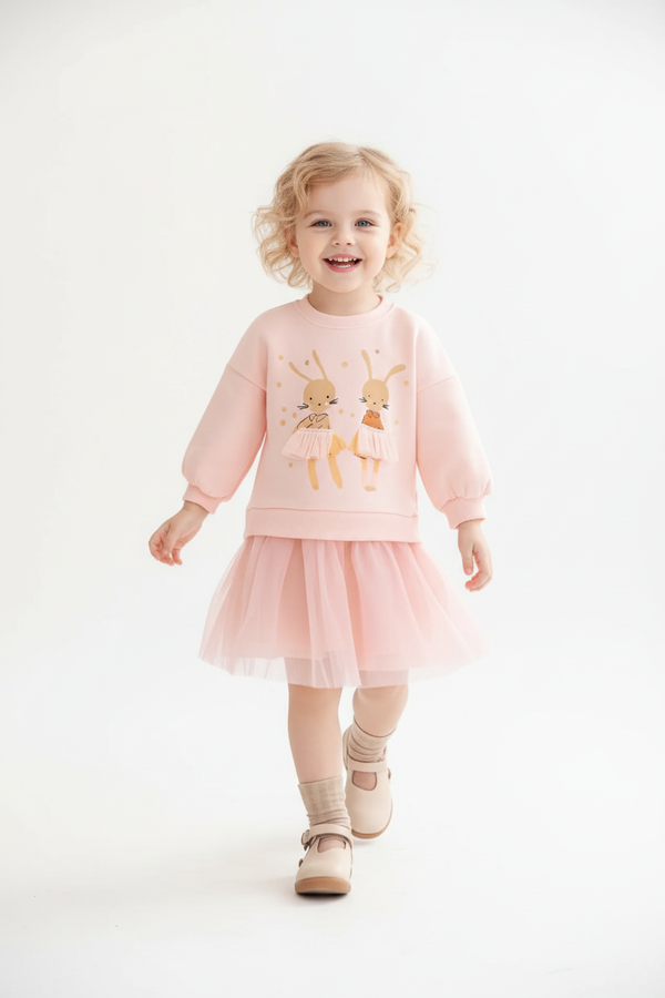 Petite fille en mouvement portant tenue complète rose poudré : haut sweatshirt manches longues appliqué lapin 3D avec carotte et détails pois dorés, jupe tulle multicouche rose pale, ensemble fille 100% coton pour Pâques printemps mariage - Vue plein pied angle léger
