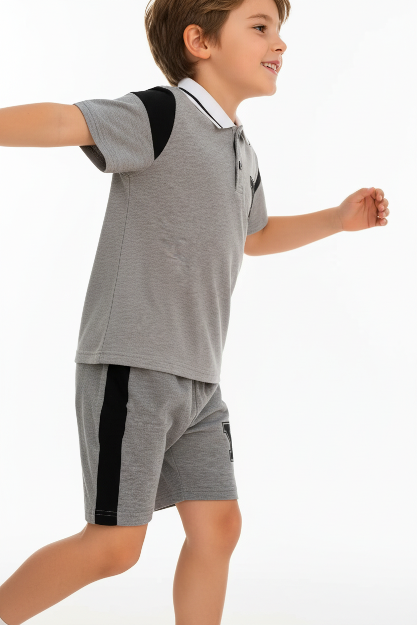 "Enfant 6 ans en pose active dynamique - Ensemble polo et short gris chiné sportif - Polo col blanc avec bordures noires contrastantes, logo Y noir sur poitrine, manches courtes avec détails noirs - Short gris coordonné avec bandes latérales noires et logo Y noir - Vue de profil latérale montrant silhouette complète de l'ensemble - Coupe athlétique moderne et confortable - Mouvement naturel et sportif - Fond blanc studio professionnel - Photo produit lifestyle premium BabyCoton Suisse - Style casual élégant