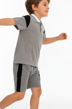 "Enfant 6 ans en pose active dynamique - Ensemble polo et short gris chiné sportif - Polo col blanc avec bordures noires contrastantes, logo Y noir sur poitrine, manches courtes avec détails noirs - Short gris coordonné avec bandes latérales noires et logo Y noir - Vue de profil latérale montrant silhouette complète de l'ensemble - Coupe athlétique moderne et confortable - Mouvement naturel et sportif - Fond blanc studio professionnel - Photo produit lifestyle premium BabyCoton Suisse - Style casual élégant