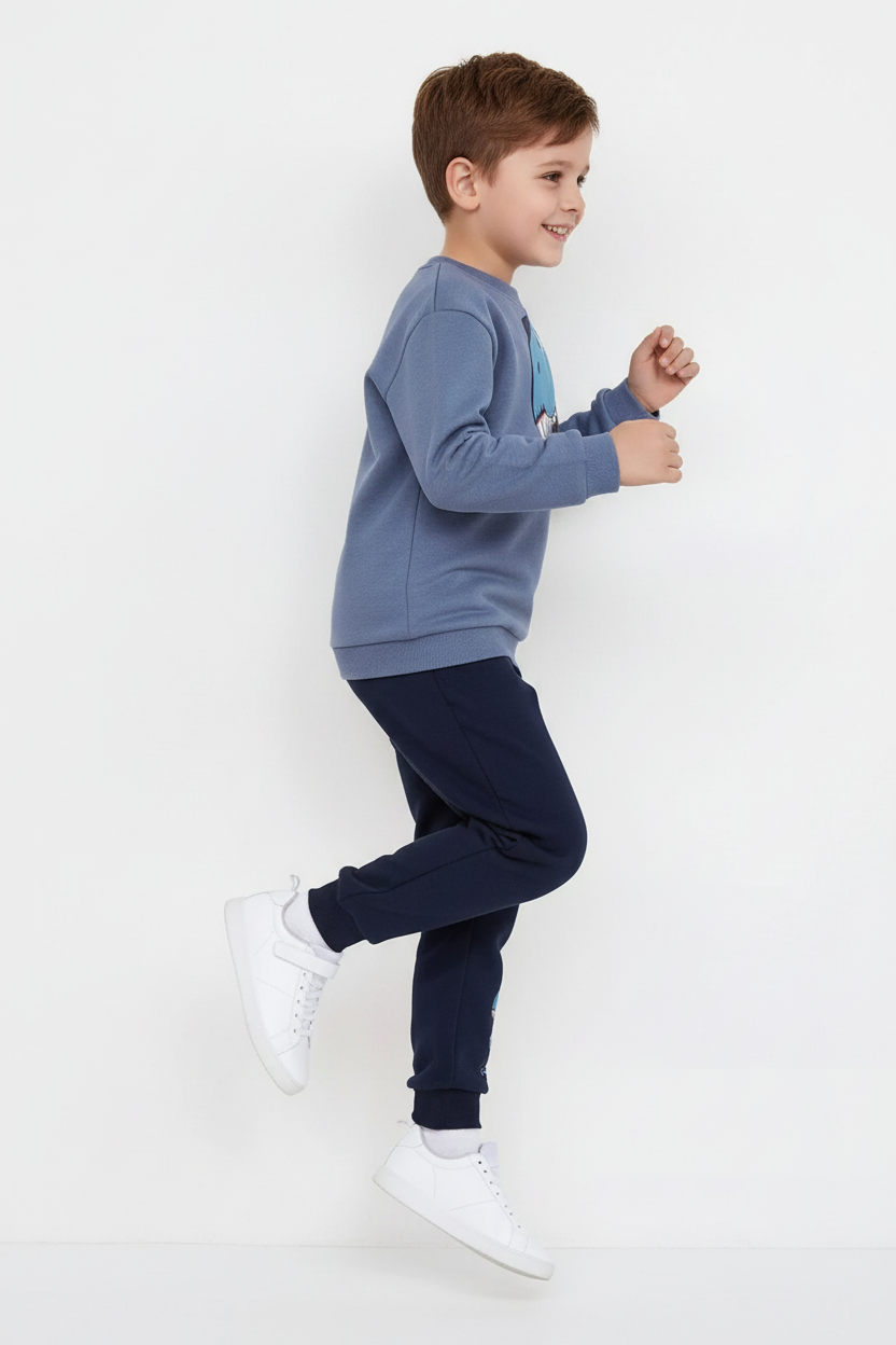 "Enfant 5-6 ans en pose active dynamique - Ensemble sweat bleu gris avec grand imprimé T-Rex bleu turquoise, pointes dinosaure 3D bleu marine sur manche, manches longues - Pantalon jogging bleu marine avec imprimé dinosaure - Vue de profil latérale montrant silhouette complète de l'ensemble - Coupe sportive confortable moderne - Mouvement naturel et aventurier - Fond blanc studio professionnel - Photo produit lifestyle premium BabyCoton Suisse - Style casual préhistorique garçon 3-8 ans"

