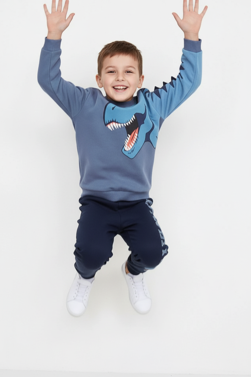 "Enfant 5-6 ans sautant de joie bras levés - Ensemble sweat bleu gris imprimé T-Rex bleu turquoise avec pointes dinosaure 3D sur manche - Pantalon jogging bleu marine avec imprimé dinosaure - Vue trois-quarts angle diagonal montrant mouvement dynamique - Tenue casual aventurière - Fond blanc studio professionnel - Photo produit lifestyle action BabyCoton Suisse - Style préhistorique énergique enfant"

