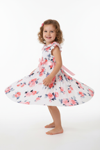 Fille en robe blanche plissée fleurie roses - pose pirouette montrant le mouvement de la jupe plissée - BabyCoton