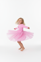 Fillette dansant et tournoyant avec bonheur en portant la robe tulle licorne rose - vue trois-quarts - fond blanc studio
