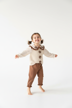 Fillette tournoyant dans ensemble haut appliqués floraux à volants et pantalon - pose dynamique joyeuse en mouvement - enfant heureuse - style fleuri romantique printanier - fond blanc studio professionnel - BabyCoton Suisse
