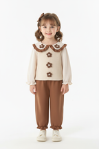 Fillette portant ensemble 2 pièces haut avec appliqués floraux délicats et volants romantiques avec pantalon coordonné - vue de face complète - style fleuri élégant printanier - fond blanc studio professionnel - vêtements fille BabyCoton Suisse
