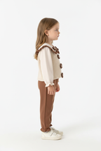 Fillette portant ensemble haut appliqués floraux à volants et pantalon - vue de profil latérale - silhouette élégante féminine - détails floraux visibles - fond blanc studio - BabyCoton Suisse
