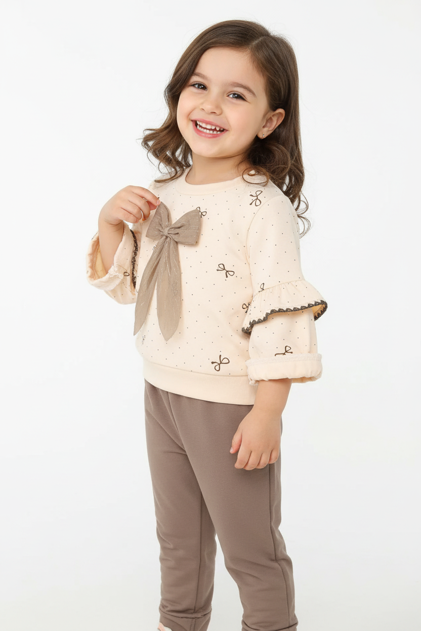 Fillette souriante portant ensemble haut nœud adorable et manches à volants romantiques délicates avec pantalon - vue trois-quarts angle - pose douce heureuse - style romantique chic - fond blanc studio - BabyCoton Suisse
