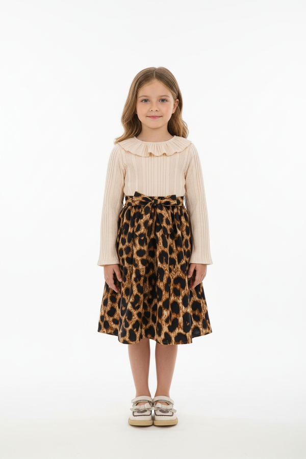 Fillette  4-5 ans portant robe élégante haut crème beige plissé grand col volant romantique - jupe imprimé léopard noir beige marron - manches longues plissées crème - ceinture nœud léopard taille - vue de face complète - sourire naturel - fond blanc studio - style sophistiqué BabyCoton Suisse
