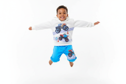 Garçon sautant en l'air avec joie en portant un hoodie blanc avec motifs monster trucks colorés et pantalon bleu assorti

