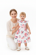 Maman agenouillée avec sa fille en robe blanche plissée fleurie roses - moment complice mère et enfant - BabyCoton