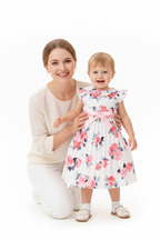Maman agenouillée avec sa fille en robe blanche plissée fleurie roses - moment complice mère et enfant - BabyCoton