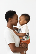 Maman et bébé garçon nez à nez en ensemble dinosaures palmiers BabyCoton — chemise polo beige dinos tropicaux et short terracotta, tendresse fond blanc
