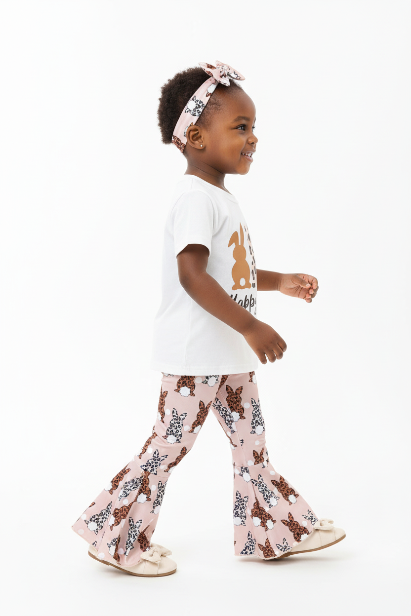 Vue de profil fillette en mouvement — ensemble Happy Easter BabyCoton, pantalon évasé rose lapins léopard en marche et bandeau nœud, fond blanc
