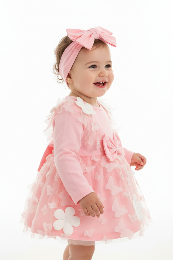 "Bébé fille 18-24 mois en pose mignonne - Robe rose poudré avec appliqués papillons blancs 3D, fleurs blanches sur épaules, nœud rose taille, jupe tulle rose multicouches avec papillons - Bandeau élastique rose avec nœud assorti - Vue de profil latérale montrant silhouette complète de la robe - Coupe romantique féminine - Mouvement naturel adorable - Fond blanc studio professionnel - Photo produit lifestyle premium BabyCoton Suisse - Style féerique jardin enchanté bébé fille 6-24 mois"