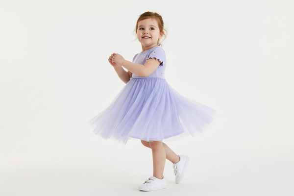 "Robe tulle manches courtes brodée pose dynamique - Tulle superposé et broderie visible - Robe affichée en mouvement fond blanc - Style féerique élégant - Photo studio professionnelle - Qualité premium BabyCoton Suisse"